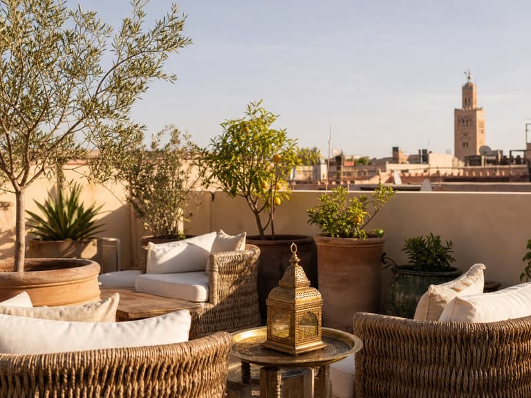 Terrasse du riad avec fauteuils en rotin, lanternes, plantes et vue sur Marrakech